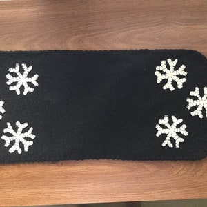May include: Black felt table runner with white snowflake embellishments. The runner has a scalloped edge.