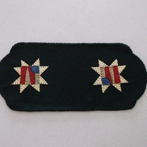 May include: A black felt table runner with two embroidered stars featuring a red, white, and blue patchwork design.