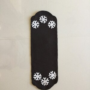 May include: A black felt table runner with a scalloped edge and white snowflake designs.