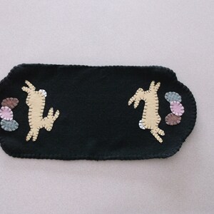 May include: A black felt table runner with two embroidered bunnies and a cluster of colorful felt circles.