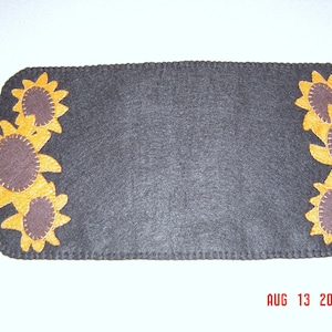 May include: A gray felt table runner with a scalloped edge and a border of yellow felt sunflowers. The sunflowers have brown centers and are arranged in a row around the edge of the runner.