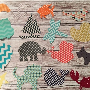 May include: A collection of colorful paper cutouts in various shapes, including animals, a sailboat, and a balloon. The cutouts feature patterns like polka dots, chevrons, and geometric designs. The background is a light wood grain.