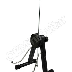 May include: Black guitar stand with a curved top and adjustable height. The stand has a black base and support arms with rubber ends to hold the guitar. The stand is designed to hold a guitar upright.