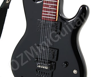 Può includere: Chitarra elettrica nera con tastiera in legno rosso e una tracolla. La chitarra è su un supporto nero. "OZMiniGuitar" è stampato sul corpo della chitarra.