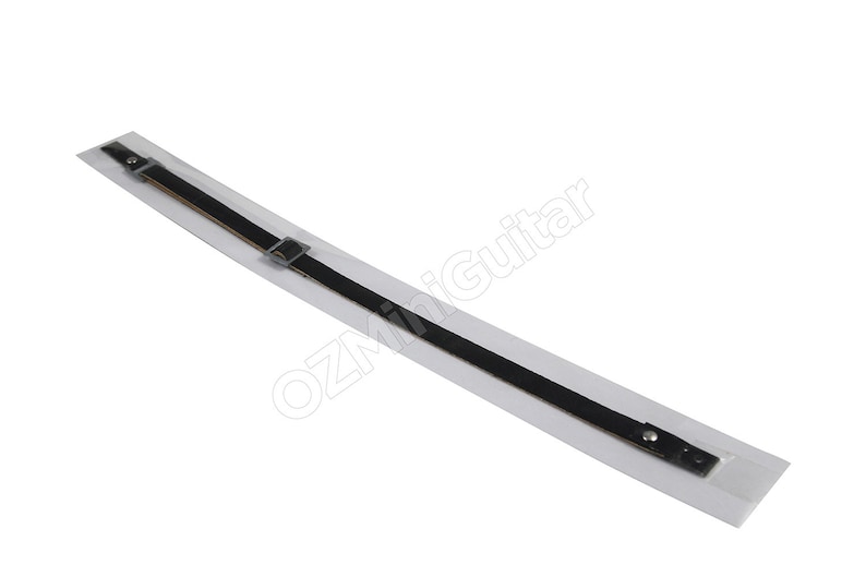 May include: A long, thin black strap with a metallic buckle and a silver-toned stud fastener at one end. The strap is mounted on a rectangular white backing card that features the text OZMiniGuitar printed in a light gray, slanted font.