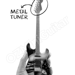 May include: A miniature electric guitar featuring a black and white striped body, a long neck with frets, and a headstock with metal tuners. The image includes a hand-drawn circle around the headstock with an arrow pointing to the text METAL TUNER.