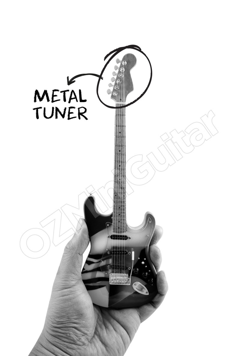 May include: A miniature electric guitar featuring a black and white striped body, a long neck with frets, and a headstock with metal tuners. The image includes a hand-drawn circle around the headstock with an arrow pointing to the text METAL TUNER.