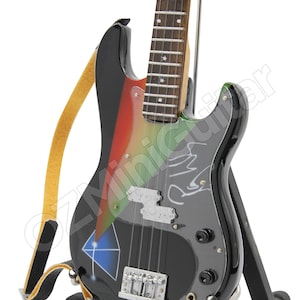 Puede incluir: Un bajo negro con pintura de colores arco&iacute;ris y una golpeador plateado. El bajo est&aacute; en un soporte negro y tiene una correa de cuero marr&oacute;n.