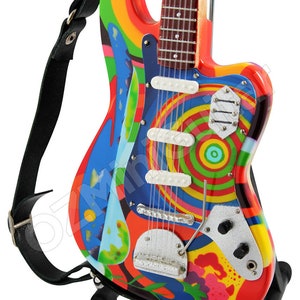 May include: A miniature electric guitar with a colorful psychedelic design. The guitar has a black strap and is on a black stand.