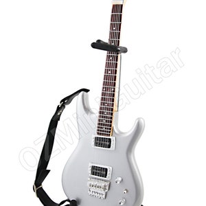 Puede incluir: Una guitarra el&eacute;ctrica plateada con una correa negra y un soporte negro. La guitarra tiene un diapas&oacute;n de palisandro y herrajes cromados.