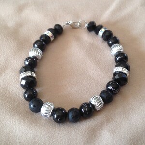 May include: A black beaded bracelet with silver accents. The bracelet features black beads with silver accents and a silver clasp.