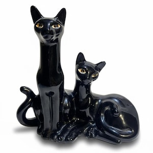 May include: A pair of black ceramic cat figurines. One cat is upright with a long neck, the other is reclining. Both cats have yellow eyes and a glossy finish. The figurines are likely decorative items.
