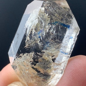 May include: A clear quartz crystal with a double termination and inclusions of blue and gold. The crystal is faceted and has a sharp point.