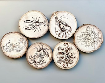 May include: Six wooden coasters with different sea creatures engraved on them. The coasters feature a seahorse, a crab, an octopus, a shrimp, a lobster, and a sea anemone.