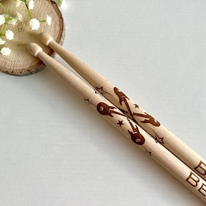 Puede incluir: Dos baquetas de madera con un diseño de guitarra marrón y la palabra "BEAUTIFUL" impresa en ellas.