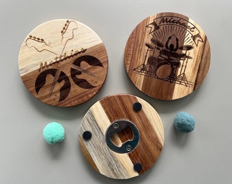 May include: Three round wooden coasters with different designs. One coaster features a guitar design with the name "Matthias" engraved on it. Another coaster features a drummer playing a drum set with the name "Michael" engraved on it. The third coaster has a bottle opener in the center and is made of different wood types.