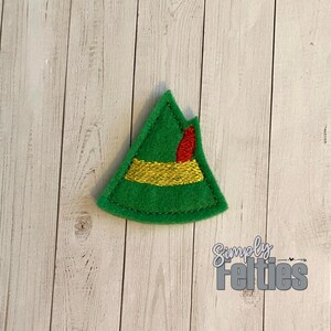 May include: Green felt elf hat with a gold band and red trim. The hat is a felt applique.