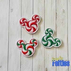 May include: Three felt Christmas ornaments shaped like Mickey Mouse ears. Each ornament is a different color combination of red, green, and white candy cane swirls.