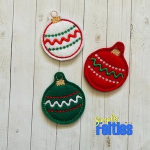May include: Three felt Christmas ornaments in red, green, and white with gold accents. Each ornament has a wavy design and a small loop at the top.