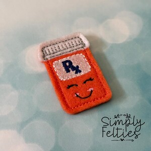 May include: Orange felt pill bottle with a white lid and a smiling face. The bottle has an "Rx" symbol on the front.