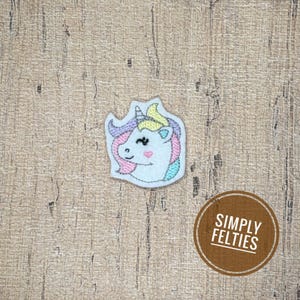 May include: An embroidered patch featuring a white unicorn head with a yellow horn, a pink heart on its cheek, and a mane composed of pastel purple, pink, yellow, and blue threads. The patch has a white border and is shaped like a unicorn head.