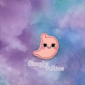 May include: Pink felt applique of a smiling stomach with eyelashes and rosy cheeks. The applique is on a purple and blue galaxy background with the text "Simply Felties".