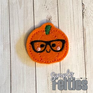 May include: A felt pumpkin with a friendly face, wearing black glasses. The pumpkin is orange with a green stem and has a stitched outline.