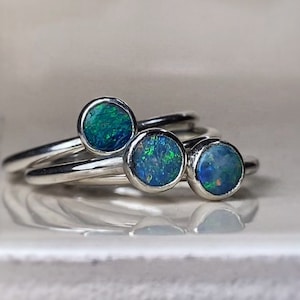 Puede incluir: Tres anillos de plata con piedras preciosas de ópalo azul verdoso. Los anillos están apilados uno encima del otro.