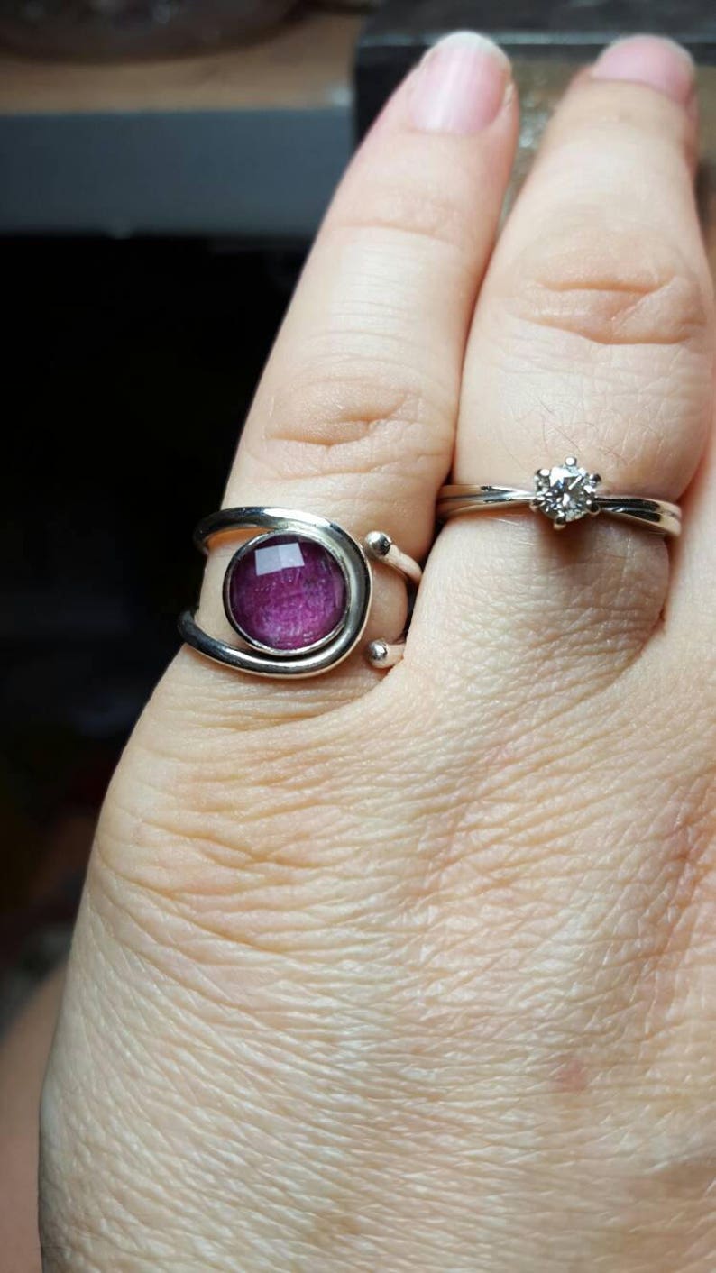 K&ouml;nnte beinhalten: Zwei silberne Ringe an einem Finger. Der Ring unten hat einen violetten Stein, der in eine silberne Fassung gefasst ist. Der Ring oben hat einen einzigen klaren Stein.