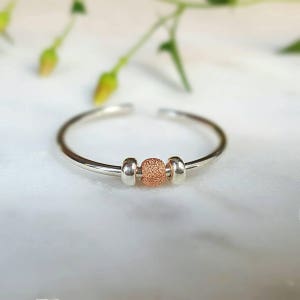 Op de afbeelding: Een zilveren ring met een getextureerde roze gouden kraal en twee zilveren kralen.