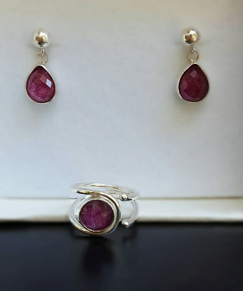K&ouml;nnte beinhalten: Ein Paar silberne Ohrringe mit einem tropfenf&ouml;rmigen rosa Stein und ein silberner Ring mit einem runden rosa Stein.