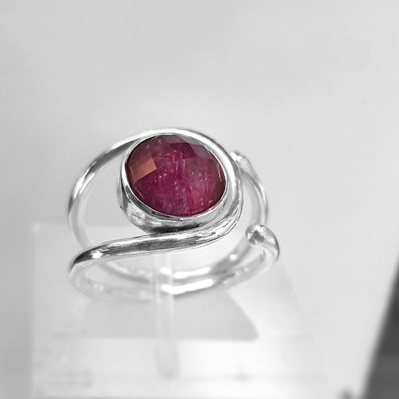 K&ouml;nnte beinhalten: Ein silberner Ring mit einem tief roten Edelstein, der in einem verdrehten Band gefasst ist.