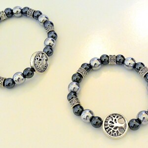 K&ouml;nnte beinhalten: Zwei Armb&auml;nder mit silbernen Perlen und einem silbernen Anh&auml;nger in Form eines Lebensbaums. Die Perlen sind schwarz und silber.