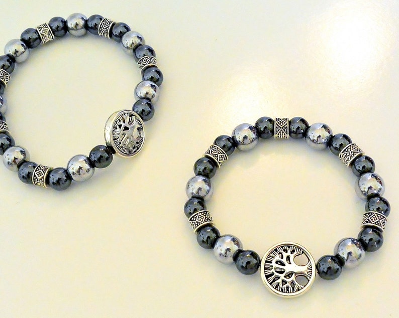 K&ouml;nnte beinhalten: Zwei Armb&auml;nder mit silbernen Perlen und einem silbernen Anh&auml;nger in Form eines Lebensbaums. Die Perlen sind schwarz und silber.