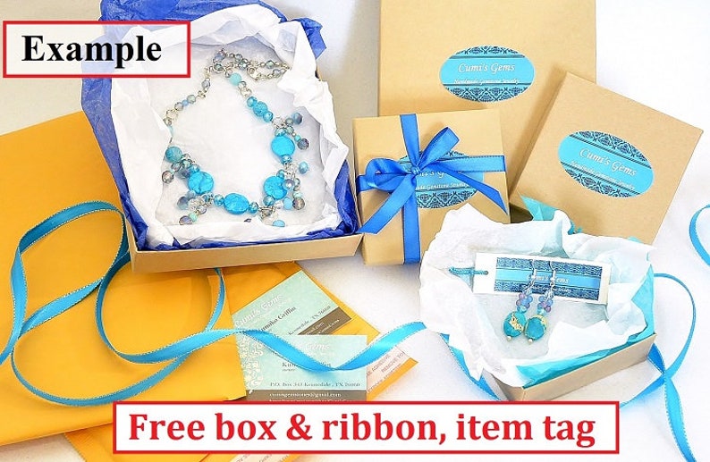K&ouml;nnte beinhalten: Beispiel f&uuml;r eine blaue und silberne Halskette und Ohrringe, verpackt in einer braunen Schachtel mit einem blauen Band. Die Schachtel ist mit "Cumi's Gems" beschriftet. Das Bild zeigt auch eine Visitenkarte und ein Etikett mit der Aufschrift "Kostenlose Schachtel & Band, Artikel-Etikett".