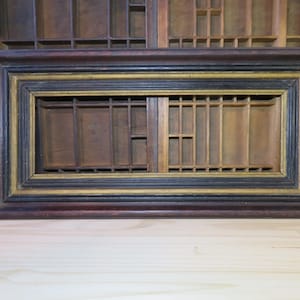 May include: A rectangular wooden frame with a dark brown finish, accented by black and gold trim. The frame features a grid-like interior design, suggesting a decorative or functional purpose. The piece is likely vintage or antique.