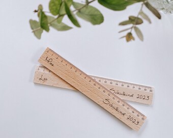 Könnte beinhalten: Zwei Holzlineale mit den Worten "Max" und "Leo" darauf. Die Lineale sind mit Zahlen von 1 bis 20 gekennzeichnet und die Worte "Schulkind 2023" sind darauf geschrieben.