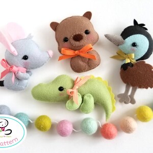 May include: A set of five felt animal plushies, including a koala, a kangaroo, an emu, a crocodile, and a garland of colorful felt balls. The plushies are all wearing bows and have embroidered eyes. The garland is strung on a white thread.