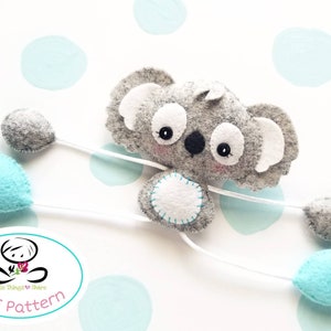 May include: A gray felt koala holding four balloons. Two balloons are gray and two are light blue. The koala has white ears and a white belly with a circle of stitching. The koala is attached to the balloons with white string. The image includes the text "Little Things to Share PDF Pattern".
