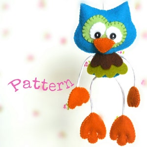 Peut inclure: Un hibou en feutre bleu avec des accents verts, bruns et orange. Le hibou a de grands yeux blancs et un long bec orange. Le hibou est suspendu &agrave; une ficelle blanche et a des pieds en feutre orange.