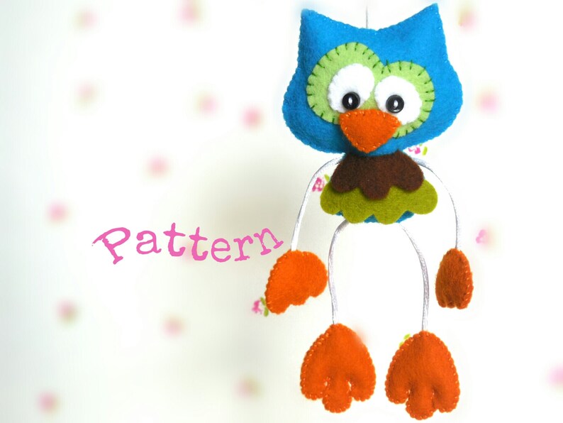 Peut inclure: Un hibou en feutre bleu avec des accents verts, bruns et orange. Le hibou a de grands yeux blancs et un long bec orange. Le hibou est suspendu &agrave; une ficelle blanche et a des pieds en feutre orange.