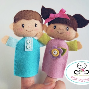 Könnte beinhalten: Zwei Fingerpuppen aus Filz, ein Junge und ein Mädchen. Die Jungenpuppe trägt ein blaues Hemd mit weißen Knöpfen und die Mädchenpuppe trägt ein rosa Kleid mit einer lila Blume und einem gelben Knopf. Die Puppen befinden sich auf einem Finger und der Hintergrund ist weiß.