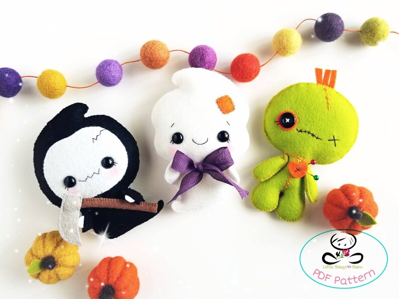 May include: Three felt Halloween character patterns: a ghost, a grim reaper, and a voodoo doll. The patterns are on a white background with a string of colorful felt balls and small felt pumpkins.