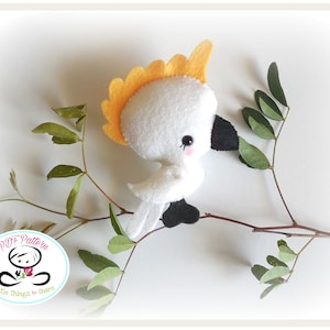 May include: A white felt cockatoo with a yellow crest perched on a branch with green leaves. The cockatoo has black eyes and a black beak. The text "PDF Pattern Little Things to Share" is on a blue and white circle.