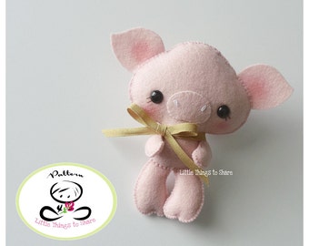 May include: A pink felt pig with black eyes and a gold ribbon around its neck. The pig is a handmade toy and is part of a pattern for making felt toys.