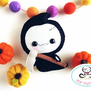 May include: A black and white felt plush toy of the Grim Reaper holding a scythe. The toy is sitting on a white surface with orange and yellow felt pumpkins.