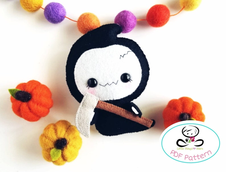 May include: A black and white felt plush toy of the Grim Reaper holding a scythe. The toy is sitting on a white surface with orange and yellow felt pumpkins.