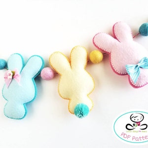 Peut inclure: Une guirlande de lapins en feutre avec trois lapins en bleu, jaune et rose. Chaque lapin a un nœud et une queue en pompon. La guirlande est enfilée avec des boules de feutre colorées. PDF Pattern.