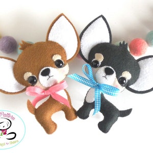 May include: Two felt Chihuahua dog ornaments, one brown and one black, each with large ears and a ribbon bow. A string of colourful felt balls is in the background. The ornaments are handmade.