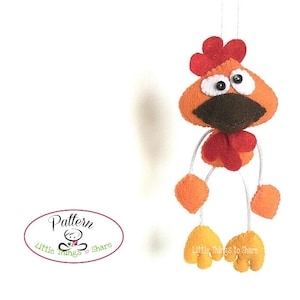 May include: A felt orange and red rooster with brown beak and large black eyes. The rooster is hanging from a white string and has white legs with yellow feet. The text "Little Things to Share" is on the bottom of the image.